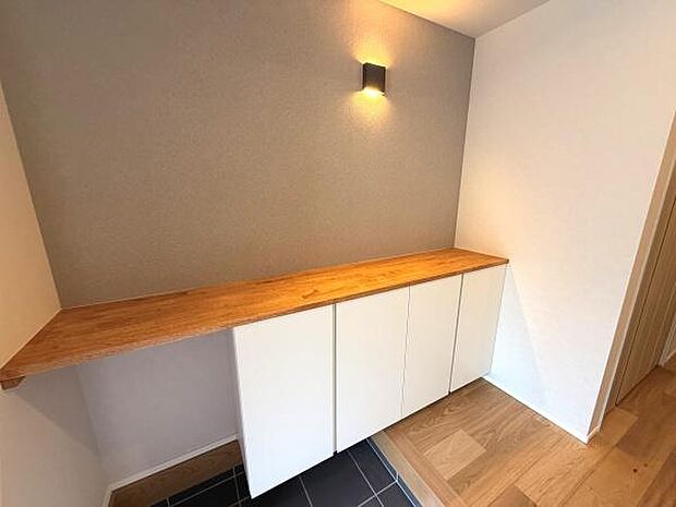 木目調のカウンターと白い扉の組み合わせが印象的な空間です。壁付の照明がアクセントになっています。床の切り替えが空間の印象を引き立てています。収納スペースも充実している点が魅力です。