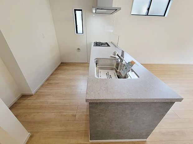 ナチュラルなフローリングと調和したキッチンです。窓から自然光が入り明るい空間を演出しています。シンプルで使いやすいデザインです。作業スペースもゆとりがあります。収納もしっかり確保されています。