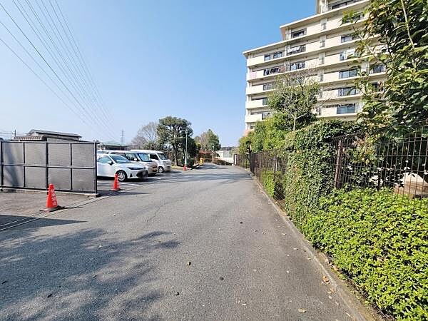 ゆったりとした駐車スペースが確保されており敷地内の緑が周囲に調和しています。道路幅も広く車の出し入れもスムーズに行えます。高層住宅の存在感が印象的な外観です。