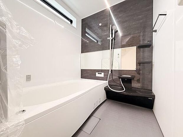 シンプルな配色で整ったデザインのバスルームです。大きな鏡が空間を広く見せます。収納棚やカウンターが機能的に配置されています。浴槽はゆったりとした形状です。窓から自然光が入り込みます。