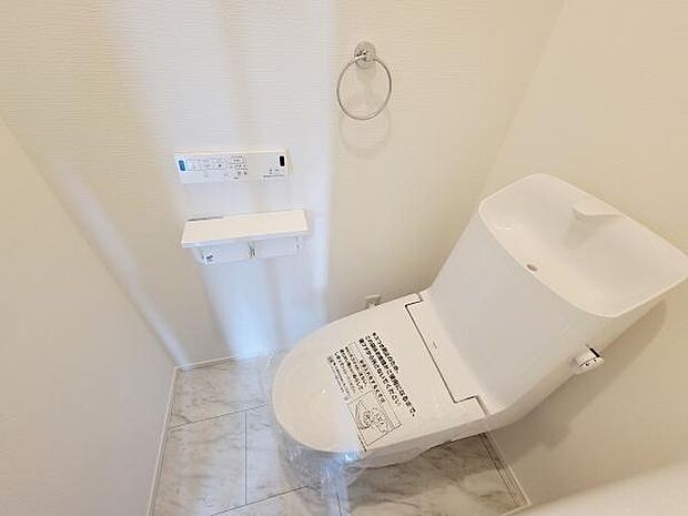 清潔感のあるホワイトを基調としたトイレ空間です。手洗い付きのタンクが備えられています。床はお手入れしやすい素材で構成されています。壁にリモコンが設置されていて操作も簡単です。