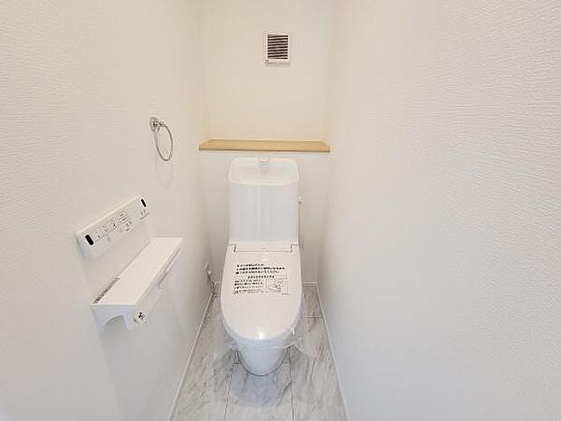 シンプルなデザインで清潔感のあるトイレです。壁付けのペーパーホルダーや棚も設置されています。コンパクトながらも無駄のないレイアウトです。床はお手入れしやすい素材となっています。