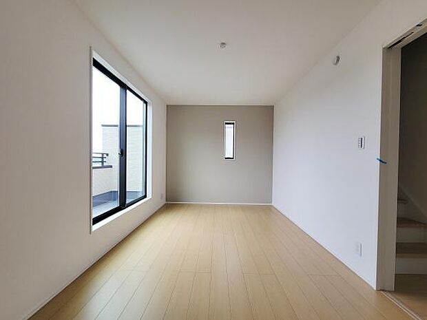 大きな窓から光が差し込む洋室です。ナチュラルなフローリングと白い壁が空間をすっきり見せます。壁面のアクセントが現代的な印象を与えています。シンプルな内装で家具配置も楽しめます。