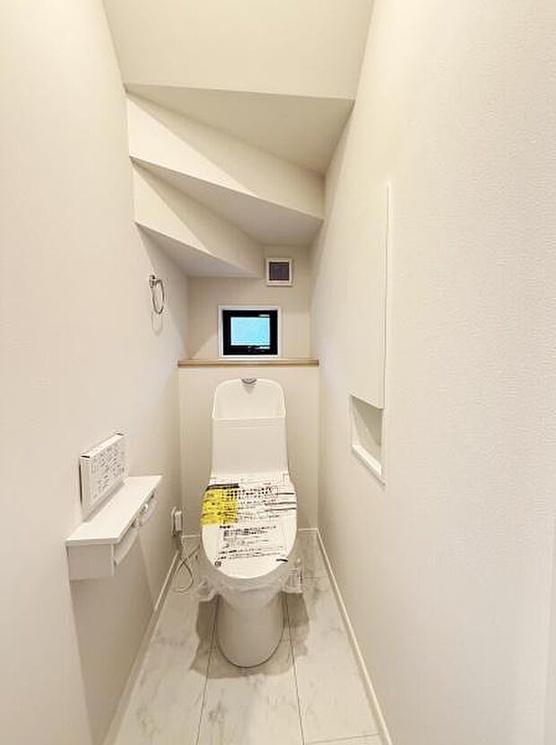 清潔感のある明るいトイレです。小窓からの自然光が空間に広がります。壁の収納スペースがすっきりとしています。床はシンプルなデザインで清掃もしやすい印象です。落ち着いた色合いで統一されています。