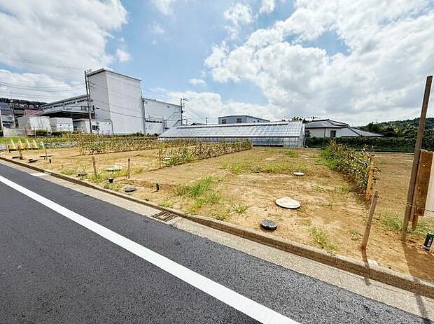 現地写真では平坦な土地が広がり区画がしっかりと確保されています。前面道路は舗装されていて車両の出入りもスムーズに行えます。明るい空が広がり周囲の建物との距離感も感じられる一枚です。