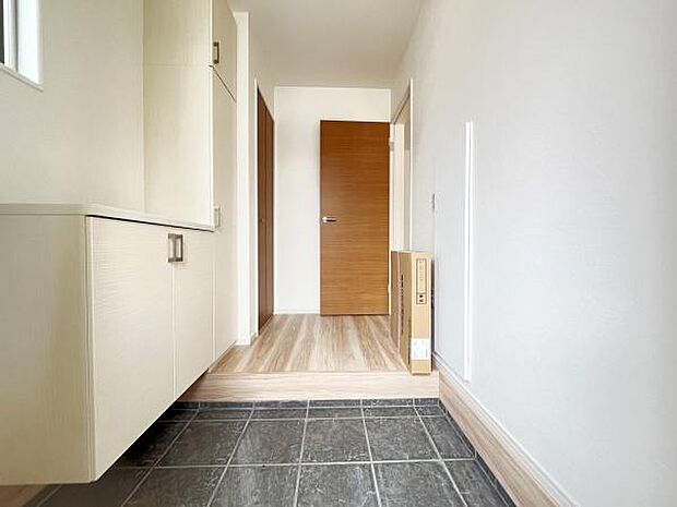 明るい空間が広がる玄関です。収納スペースが設けられており整理整頓しやすい造りになっています。落ち着いた色味のフローリングとタイル床が調和しています。ドアや建具もシンプルなデザインで統一感があります。