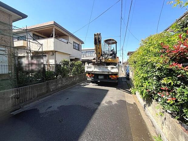 青空の下前面道路がしっかりと整備されています。周囲には住宅が立ち並び落ち着いた雰囲気が感じられます。両側に植栽が施されており自然を感じることができます。現地の様子や道路幅などもご確認いただけます。