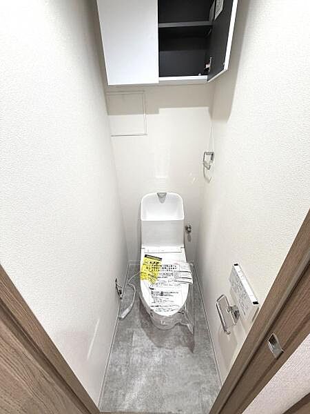 トイレには収納棚が設置されており整理整頓がしやすい空間です。床材が落ち着いた色合いで清潔感があります。ドアや壁面も明るいカラーでシンプルなデザインが特徴です。