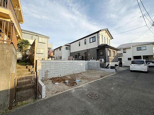前面道路が広く車の出し入れがしやすい現地写真です。周囲は住宅が立ち並び落ち着いた街並みが広がっています。道路との高低差が少なく敷地利用もスムーズです。清潔感のある現地の様子がよくわかります。