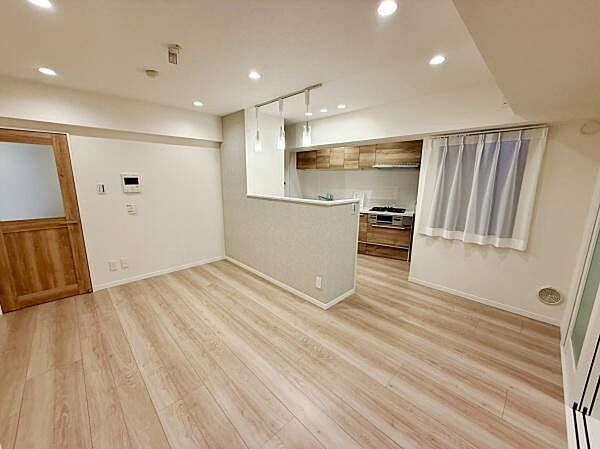 リビングは明るい照明が設置され室内全体がすっきりとした印象です。ナチュラルな木目調のフローリングが空間に調和しています。キッチンとの仕切りがあり生活空間が分かれています。