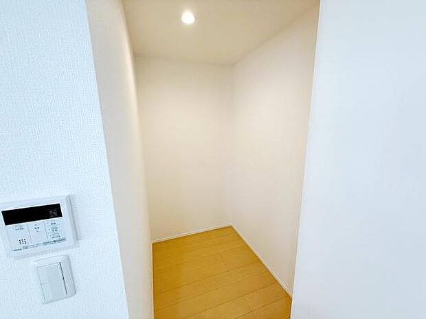 室内にスッキリとした収納スペースがあります。明るい照明が付いていて手元も見やすい仕様です。壁や床はシンプルな色合いで使い勝手に幅が広がります。入口付近にはスイッチ類もまとまっていて便利です。