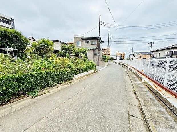 道路沿いには植栽が整えられており周辺には住宅が立ち並んでいます。道幅は比較的広く車の通行もスムーズに見受けられます。落ち着いた街並みが広がっており歩道も確保されています。周囲は明るい雰囲気です。