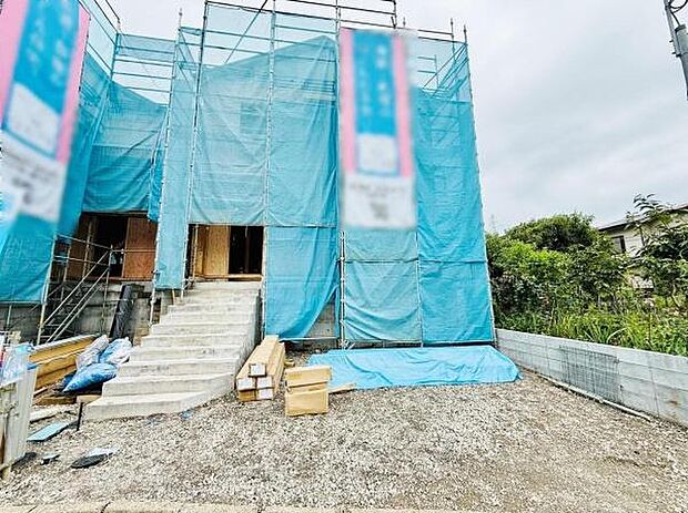 現在建築中の物件で前面には広々としたスペースが確保されています。シンプルな外観が特徴的で周囲には自然も感じられます。資材なども整理されており今後の完成が期待されます。現地の様子がよく分かる写真です。