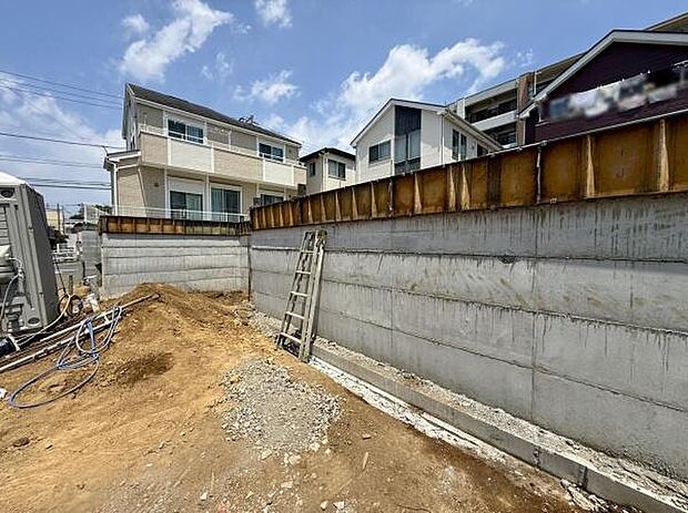 現地の様子をしっかりと確認できる写真です。コンクリート擁壁がしっかりと設置されており作業の進捗が分かります。周辺には住宅も多く新しい生活のイメージが湧きます。整備された敷地が印象的です。