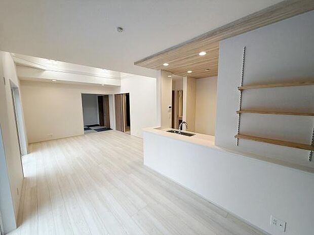 明るい色合いの床と天井が空間を広く感じさせます。キッチンからリビング全体が見渡せるつくりです。オープンな印象の棚もアクセントとなっています。やわらかな照明が室内をやさしく照らします。