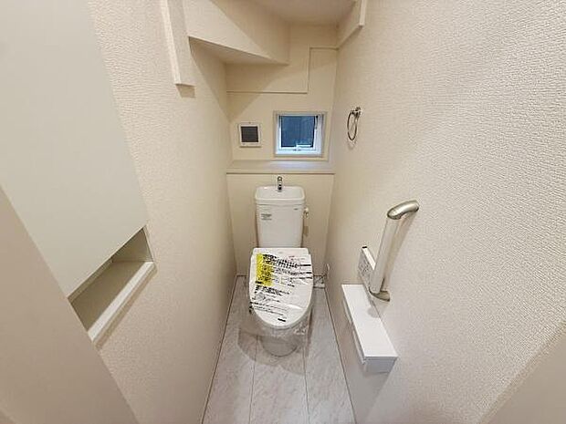 小窓が設けられており自然光が入るトイレです。ペーパーホルダーや手すりなど使い勝手を考慮した設計になっています。スペースを有効活用した収納棚が備え付けられています。清潔感のある明るい内装です。