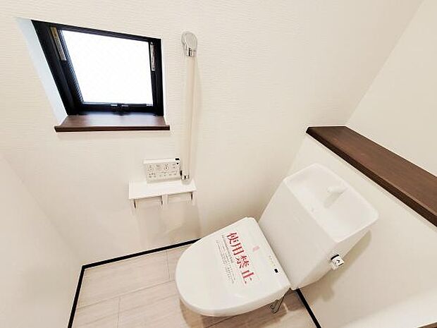 窓からの採光が明るいトイレです。壁付リモコンが配置されています。収納スペースとして便利なカウンター付きです。床は落ち着いた雰囲気です。清潔感のある空間です。