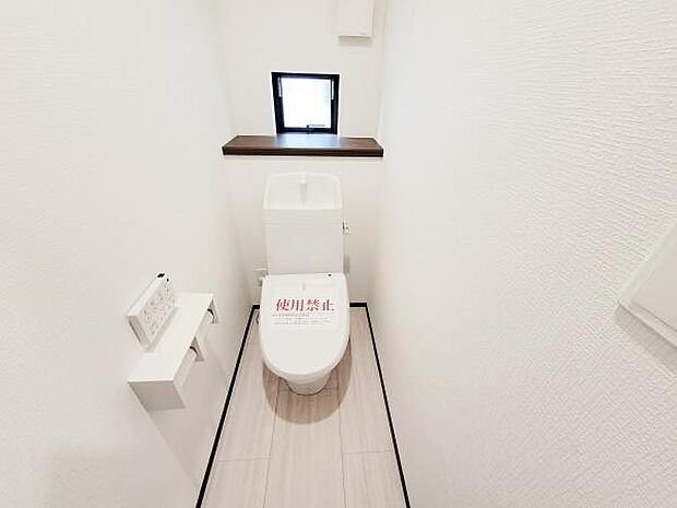 明るく清潔感のあるトイレです。小窓があり換気がしやすい設計です。手洗い付きのタンクが備え付けられています。床や壁の色合いが落ち着いた雰囲気を演出しています。壁面には収納スペースも確保されています。