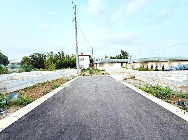 前面道路がしっかりと舗装されており車の出入りにも配慮された現地写真です。広々とした敷地スペースが確保されています。現地の様子が分かりやすく撮影されています。周囲の緑も感じられる環境です。