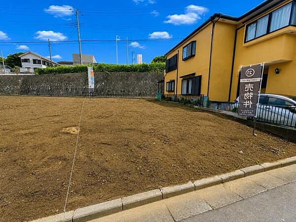 前面道路に面した現地写真で視界が広く感じられます。周囲は落ち着いた住宅が建ち並んでいます。道路との高低差が少なく敷地全体が見通しやすいです。整地済みで土地の形状が分かりやすい写真です。