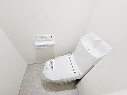 シンプルで清潔感のあるトイレです。操作しやすい壁付けパネルが設置されています。タンク上部には手洗いスペースも付いており便利です。床はお手入れしやすい素材になっています。