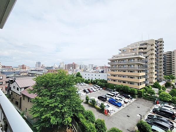 バルコニーから広がる眺望が開放感を演出します。周囲には高層の建物が並び都市らしい景色が楽しめます。駐車場や緑も視界に入り安心感があります。明るい空が全体を包み込む印象です。