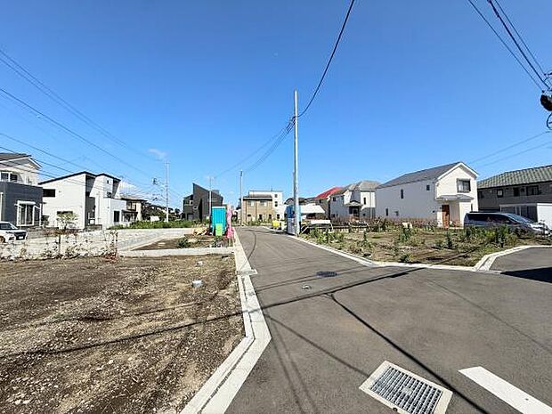 前面道路含む現地写真です。幅のある道路が続き住宅街らしい落ち着いた雰囲気が広がっています。周囲には新しい住宅が立ち並び区画も整っています。視界も開放的で陽当たりの良さが感じられます。