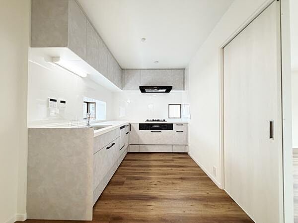 シンプルで明るいキッチンが特徴です。木目調の床と白い壁が調和し空間をすっきりと見せています。収納も多めで使い勝手に配慮されています。大きな調理スペースが確保されています。