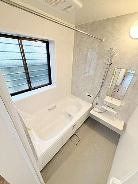 浴室には大きな窓が備わっており換気もしやすい設計です。シャワーや鏡カウンターも揃い使いやすさを感じます。浴槽と洗い場がすっきりとレイアウトされています。グレーのアクセントパネルで落ち着いた雰囲気です。