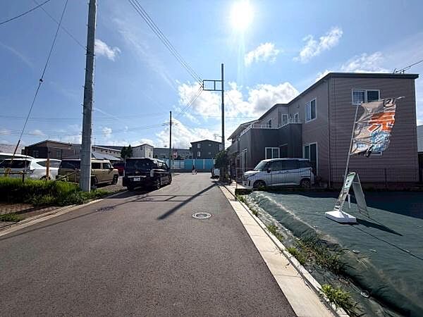 整備された道路沿いに位置し周囲には戸建て住宅が並ぶ落ち着いた街並みです。電柱や配線が整然としていて整った環境が印象的です。住宅の前面には駐車スペースや開けた空間が確保されています。