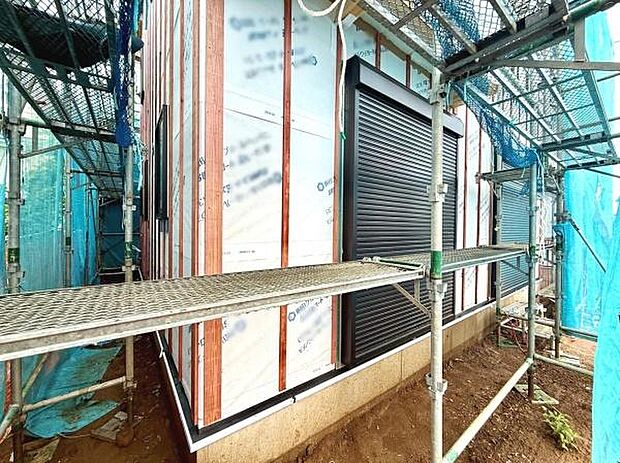 建築中の様子がわかる写真です。外壁工事の進行状況が確認できます。しっかりと養生シートで覆われており丁寧な作業が感じられます。窓にはシャッターが設置されています。