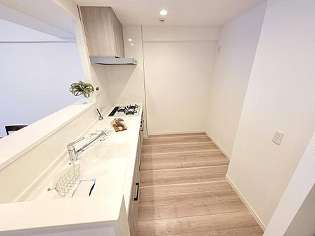 白を基調とした明るいキッチンです。作業スペースが広くお手入れがしやすいシンプルな設計です。カウンターがあり開放感があります。収納も充実しており効率的に使用できます。