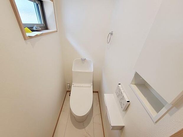 清潔感のある白を基調としたトイレです。小窓から自然光が入り換気も行いやすい設計です。小物を置けるカウンターや収納スペースも備えています。床や壁も手入れがしやすい仕様となっています。
