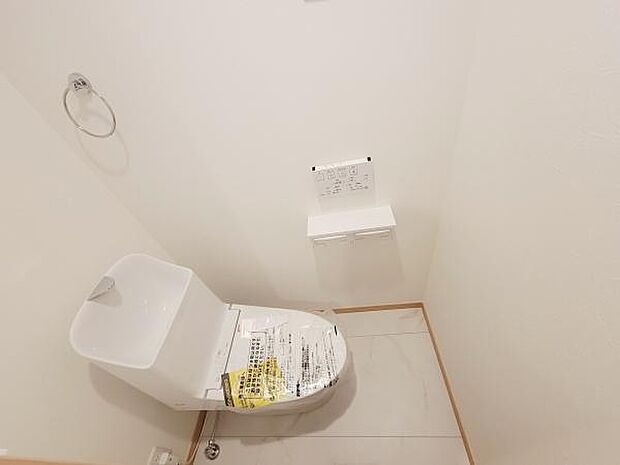 シンプルで清潔感のあるトイレ空間です。タオルリングやペーパーホルダーが備え付けられています。床や壁の色合いも明るく全体的にすっきりとした印象です。収納も使いやすい設計となっています。
