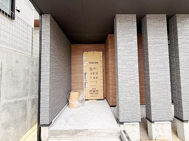 シックな色合いの外壁が印象的な玄関です。直線的なデザインがすっきりとした外観を演出します。雨除けに配慮された屋根付きのアプローチになっています。広めのスペースでゆとりを感じられます。