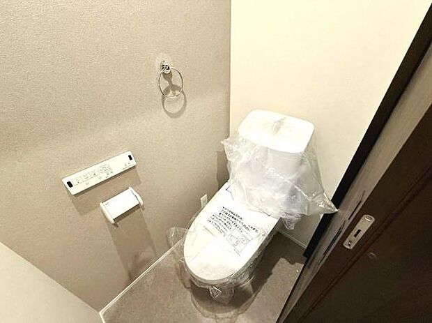 シンプルなデザインのトイレです。手洗い器一体型で使いやすい仕様となっています。壁面にはペーパーホルダーやタオルリングが設置されています。床や壁も落ち着いた色合いでまとめられています。