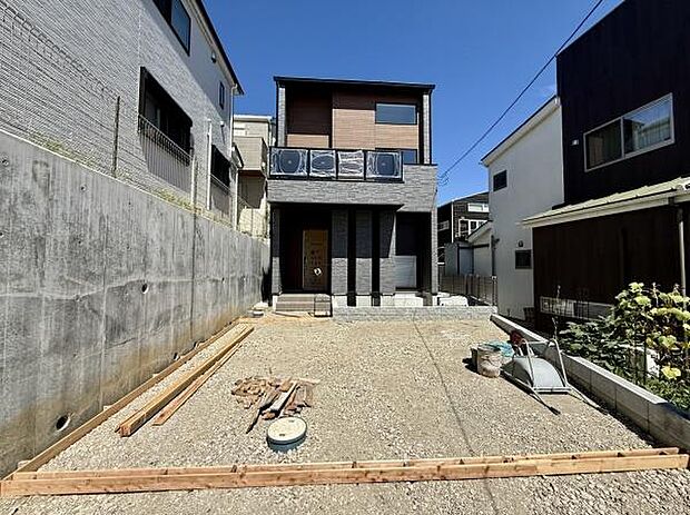 モダンな外観が洗練された印象を与える住宅です。二階のバルコニーが特徴的で広々とした開放感が感じられます。落ち着いたダークトーンの外壁が周囲と調和しています。存在感のある三本柱が目を引くデザインです。