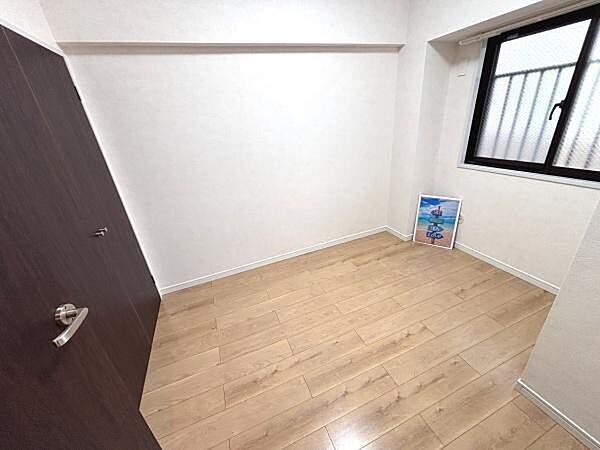 落ち着いた色合いのフローリングが広がる洋室です。窓からの採光で明るさが感じられます。壁面もシンプルで使いやすいレイアウトです。ドアや窓のデザインもアクセントになっています。