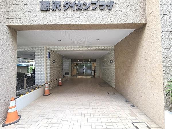 広々としたエントランスが印象的です。屋根付きで天候に左右されずに出入りできます。タイル張りの床が清潔感を演出しています。エントランス奥にはガラス扉が設けられ開放感があります。
