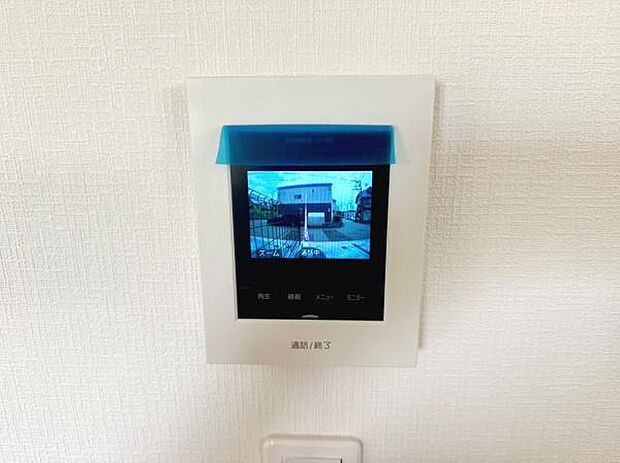 壁に設置されたモニター付きインターホンが備わっています。来訪者の確認が可能な設備です。モニターは視認性に配慮したデザインです。清潔感のある白い壁とよく調和しています。