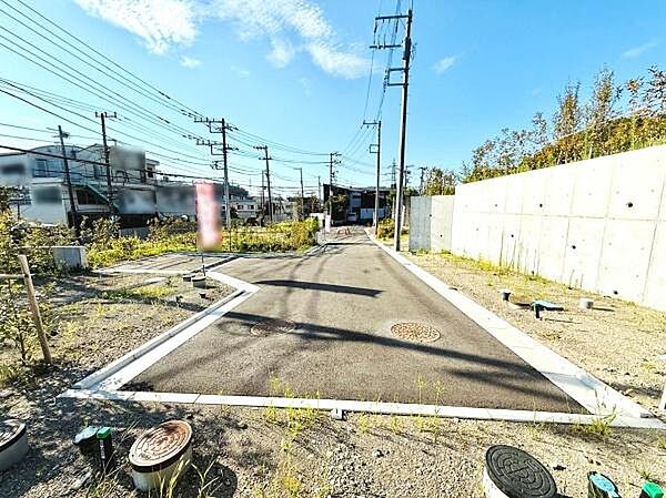 前面道路が広々としており開放感のある現地写真です。電柱や配管も整備されていて周囲の景観がすっきりしています。道路面が舗装されているため快適に利用いただけます。晴れの日の写真で明るい印象です。