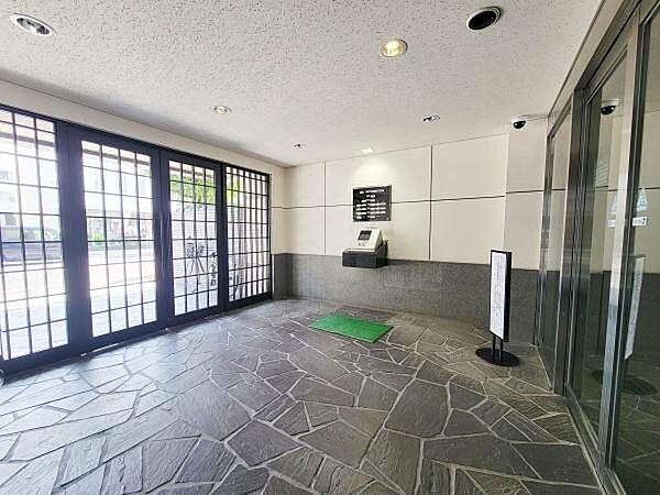 明るい光が差し込むエントランスは広々とした空間設計が特徴です。石調の床が落ち着いた雰囲気を演出しています。セキュリティ設備も設置されています。