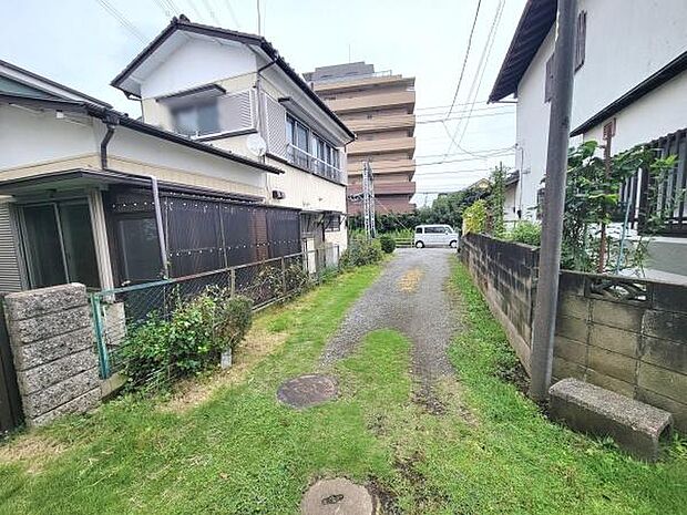 落ち着いた雰囲気の現地土地写真です。周辺は住宅が立ち並び静かな環境が広がっています。敷地前には緑があり自然を身近に感じられます。前面道路は車両の出入りに十分な広さがあります。