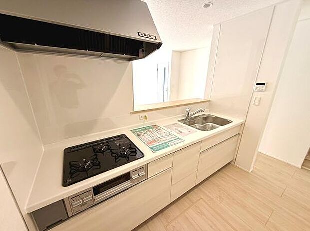 シンプルなデザインのキッチンです。使いやすい3口コンロとワイドなシンクを備えています。十分な収納スペースも魅力です。お手入れがしやすいワークトップが採用されています。清潔感のある明るいキッチンです。