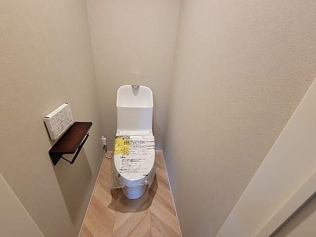 ナチュラルな色合いの壁と床が落ち着いた雰囲気を演出しています。トイレットペーパーホルダーには棚が付いており便利です。清潔感のある空間で日々の利用に適しています。
