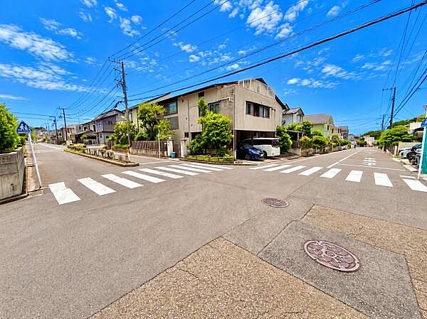 前面道路が広く車の出入りがしやすい印象です。交差点近くで見通しが良く開放感が感じられる現地写真です。