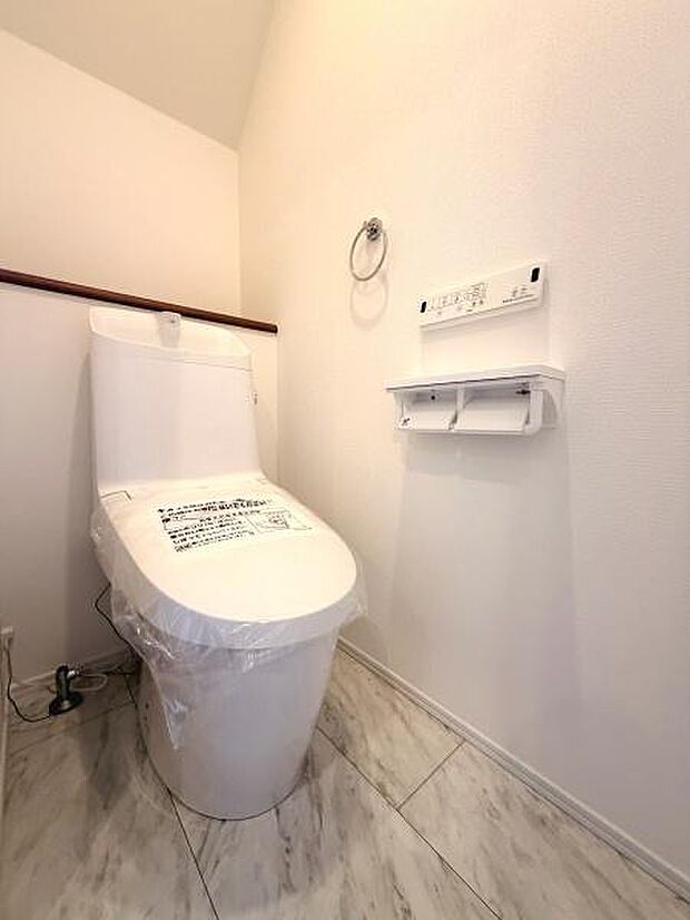 清潔感のある白を基調としたトイレです。壁付けのリモコンやペーパーホルダーが設置されており使いやすい配置です。床はお手入れしやすい素材を採用しすっきりとした空間です。収納棚も活用できます。