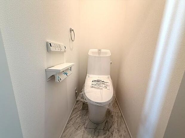 清潔感のあるトイレです。壁と床の色合いが明るく空間を落ち着いた印象にしています。ペーパーホルダーやリモコンの設置で使いやすさも考えられています。シンプルなデザインが特徴です。