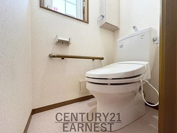 手すり付きで安心感のあるトイレ空間です。窓があるため換気もしやすく快適さを保ちやすい設計です。壁付けの収納スペースも備わっています。シンプルで清潔感のあるデザインです。