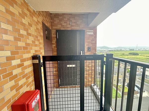 レンガ調の壁が特徴的な玄関前のスペースです。柵付きで安心感があります。周囲には開放的な眺望が広がっています。明るい外光も取り込める設計です。共用部分も清潔感があります。
